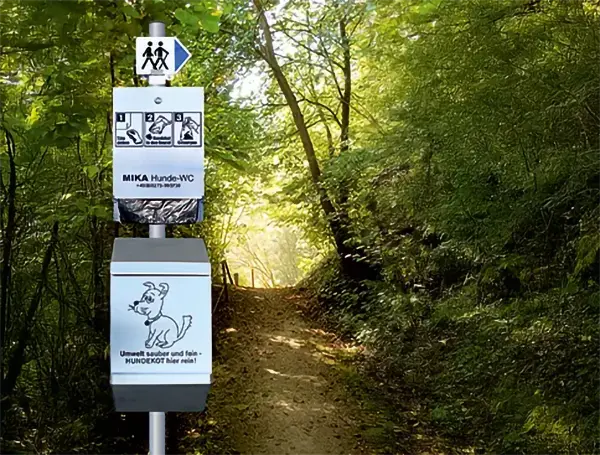 Eine Entsorgungsstation für Hundekot mit einer Anleitung neben einem Feldweg in einem sonnendurchfluteten Waldgebiet. Eine Entsorgungsstation für Hundekot mit einer Anleitung neben einem Feldweg in einem sonnendurchfluteten Waldgebiet.
